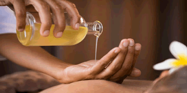 Massagista derramando óleo corporal na mão para fazer uma massagem.